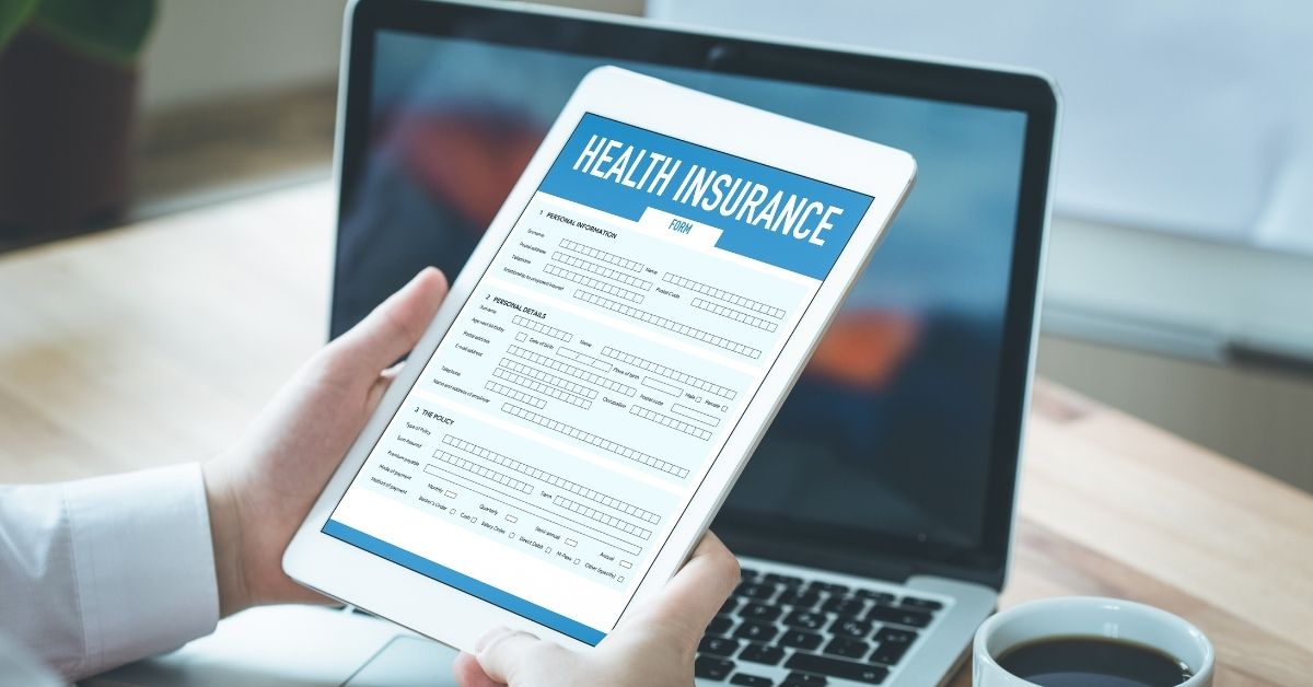 Person looking at health insurance form on tablet with a laptop and coffee on the table