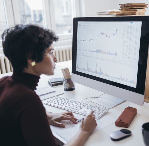 Hardworking businesswoman working with data graphs & charts displayed on a large computer screen.