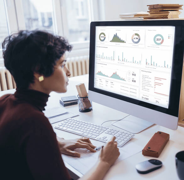 Hardworking businesswoman working with data graphs & charts displayed on a large computer screen.