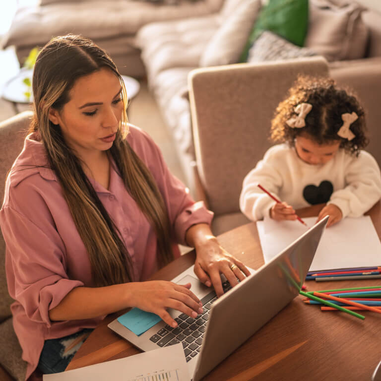 Young woman working while her daughter draws beside her at home