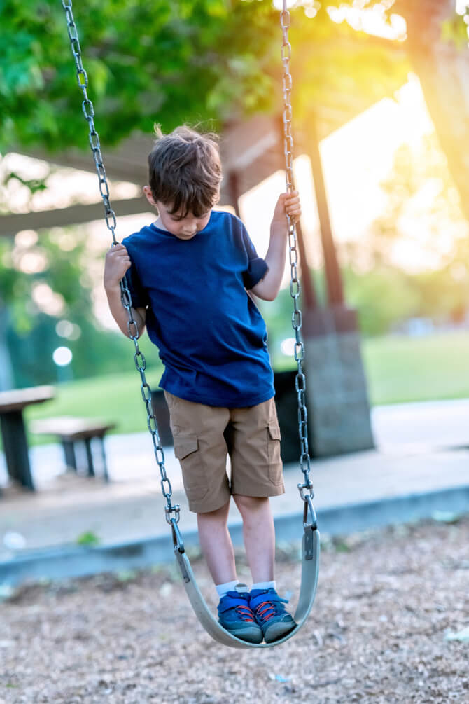 Autistic Caucasian little boy looking down swinging at the schoolyard playground