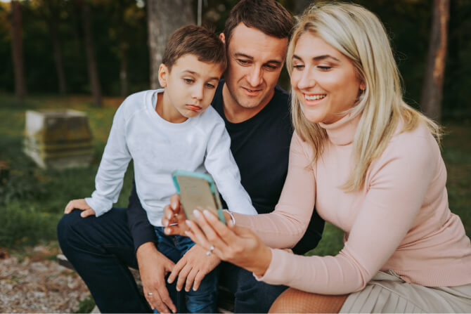 Happy mother, father, and autistic son in park looking at phone