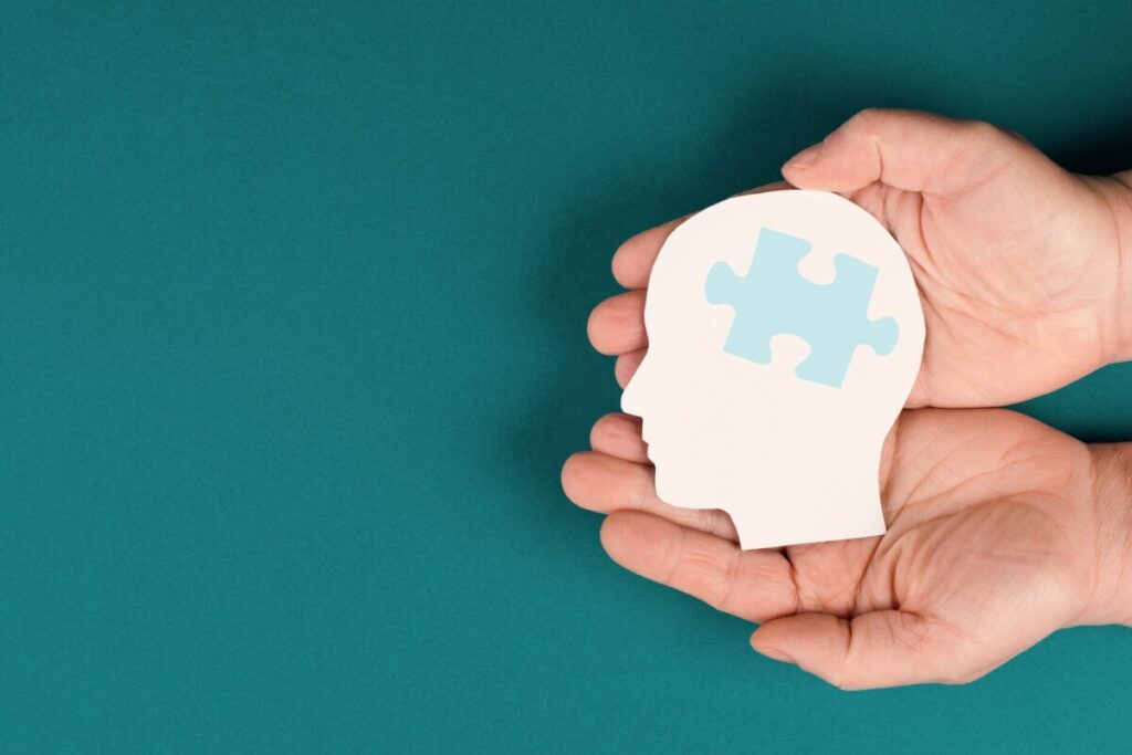 Hands cupped together holding a head with puzzle piece representing Autism
